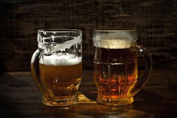 A glass of amber beer. Glasses on a wooden table. Black shabby boards on the background. Bright contrasting light and glare on the glass.