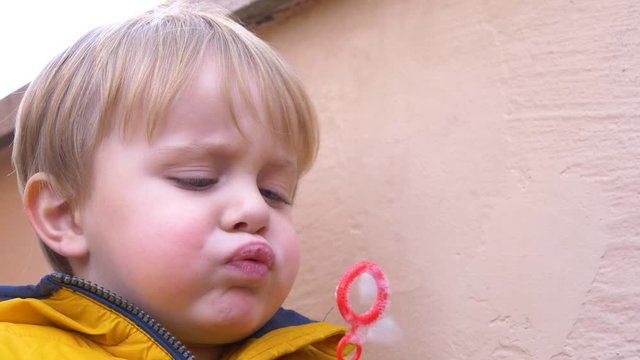 blond boy learning to blow soap bubbles on the terrace of his house