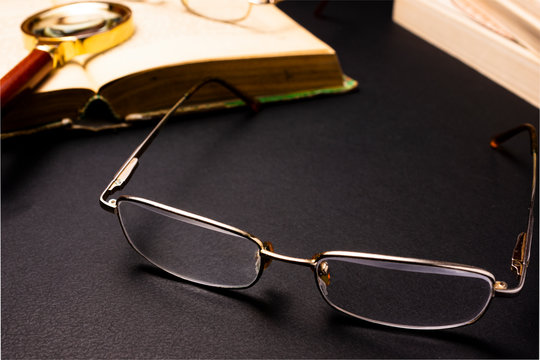 Books with glasses on black table and wooden background. High resolution image depicting reading/bokks industry.