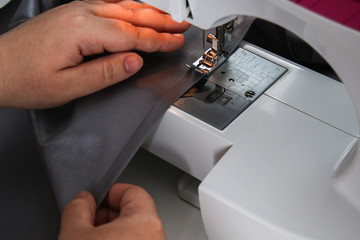 Obraz na płótnie Canvas A man hem a curtain on a sewing machine. Sewing, hobbies, hobby, home improvement.