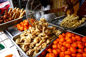Assorted deep fried street food sold at a food cart along a sidewalk.