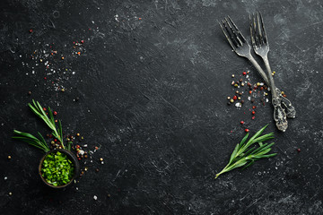 Black cooking background. Rosemary and spices on a black stone table. Top view. Free space for your text.