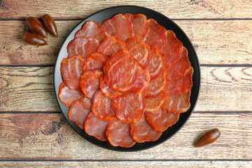 Ration of acorn-fed Iberian loin on black plate, on wooden table with acorns seen from above
