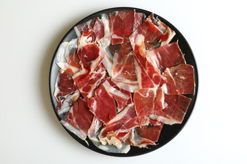 Ration of acorn-fed Iberian ham on black plate with white background
