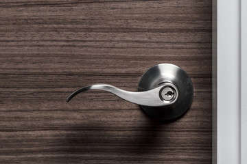 stainless steel door knob or handle with keyhole on wooden door, wave style lever handle front door knob with lock, modern interior design concept, shallow depth of field