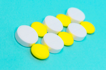 white and yellow round pills in a row on a blue background close-up layout. medical treatment copy space concept 