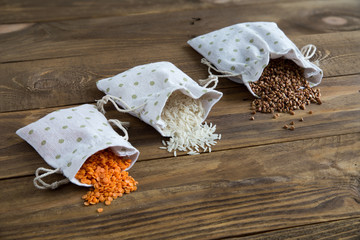 Three types of cereals buckwheat, rice and lentils in canvas bags. They lie on a wooden background. Grains are scattered on the table. Organic healthy cereals. Natural vegetarian vegetable protein.