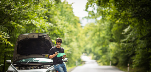 Handsome young man calling for assistance with his car broken down by the roadside