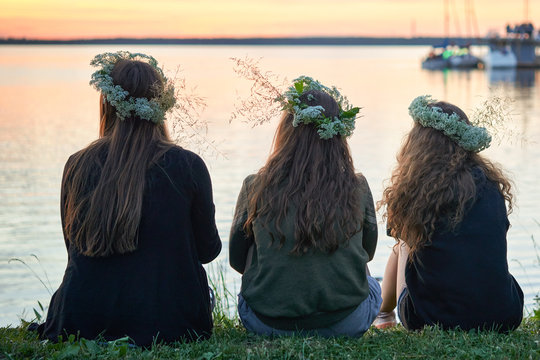 Three girls with wreaths of wild flowers by the lake. An evening at Saint John's Eve by the lake.