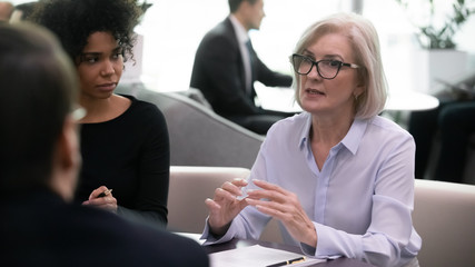 During group formal meeting multi-ethnic business people partners colleagues gathered together in office listen middle-aged 50s leader mentor. Negotiations, corporate solutions and management concept