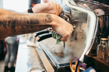 Close up shot of experienced barman or bartender hands making delicious and fresh espresso coffee drink on machine.