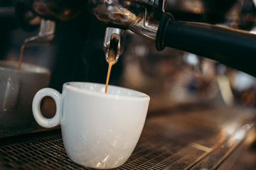 Close up shot of coffee machine pouring tasty, fresh and hot coffee in white cup.