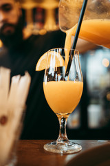 Close up shot of professional bartender pouring fresh orange juice in clean glass. Cafe bar drink concept.