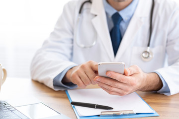 Doctor using smartphone at workplace, messaging with patient
