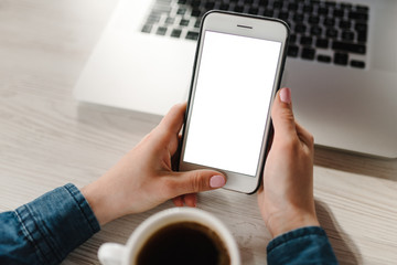 Woman's hands using empty white blank screen cell phone, working on laptop computer on table. Freelance. Work home.  Communication, technology concept. Girl checking social apps online. Top view.
