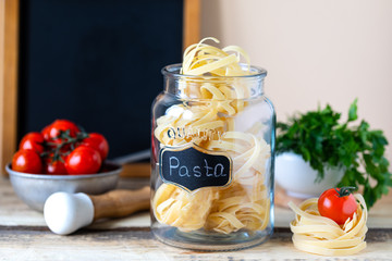 Different types of italian pasta in glass jars on a yellow wooden table. copy space