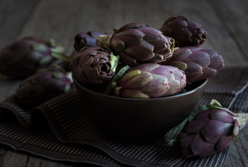 Fresh uncooked artichokes vegetables in a dark bowl, healthy food