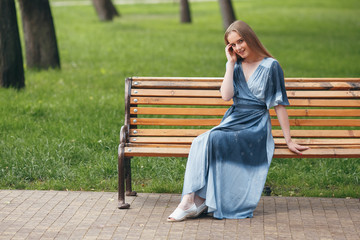 Beautiful girl sitting on a bench, brunette in a bright dress, sunny day in the park, summer holidays in the park. Sunny spring