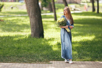 Stylish girl posing in a dress in a sunny spring park. Calm portrait of a beautiful girl standing with a bouquet in spring