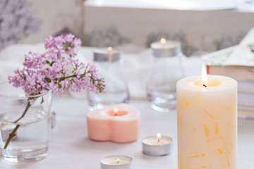 Fototapeta na wymiar Pastel room interior decor with burning hand-made candle, books, flowers. Cozy and relax concept.