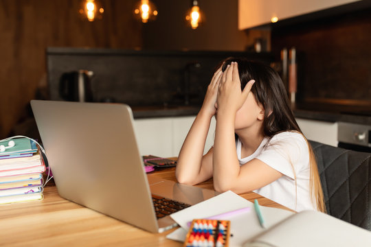 Depression and headache from online learning at home. Girl holds her head during an online lesson