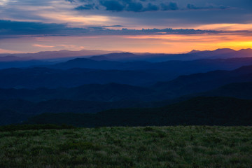 Fototapeta premium Sun Sets Behind Mountain Layers and Grassy Field