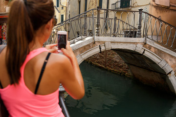 Woman tourist taking photo on smartphone in Venice, Italy. Selective focus on bridge