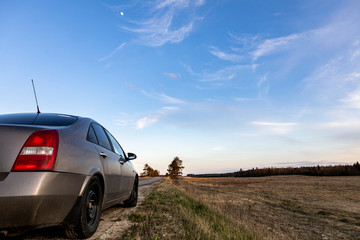 Obraz premium the automobile stands on the sidelines next to the field on the background of beautiful sunset sky. Long journey by car