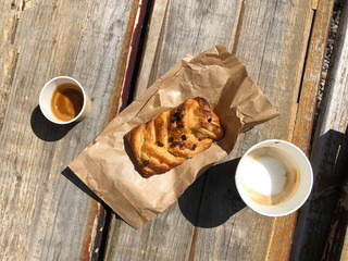 coffee cappuccino and espresso in eco friendly cardboard cups and sweet pastries for takeaway on a wooden background on the street. hard shadows and selective focus