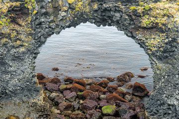 Natural volcanic rock arch in Arnarstapi in West Iceland. Basalt columns and textured rock seaside in Icelandic fjord.