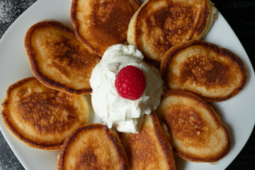 Pancakes on a white plate in the center image with raspberries and yogurt on a black background