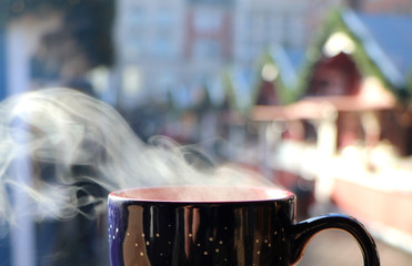 Smoke of a hot drink with Christmas market as blurry background, copy space