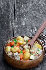 Stewed pork with vegetables in wooden bowl on rustic table