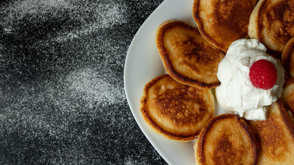 Pancakes on a white plate with raspberries and yogurt on a black background. Copy space on the left side