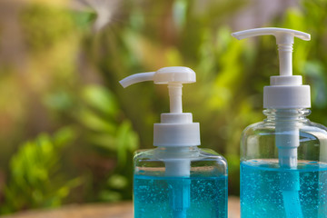 Blue alcohols gel bottle on blur green nature background and sun ray. Hand sanitizer gel in pump bottle. With copy space for text or design. Alcohols gel in 2 different size pump bottle.