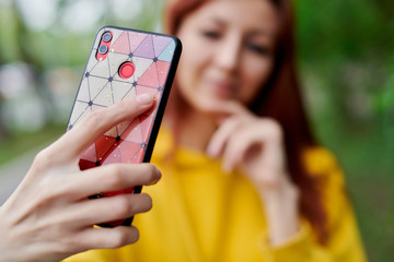Mobile phone in a beautiful case in the hand of a girl, she is out of focus and takes a selfie