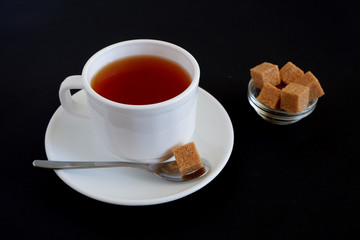 Herbal tea and pieces of brown sugar in a white mug on a black background. Suitable for advertising backgrounds and mockups