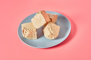 Pieces of sunflower halva lies on plate on pink background. Turkish sweets