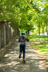 child alone in the park on a scooter in a helmet