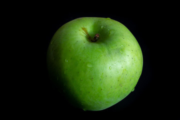 Green ripe apple with water droplets on a dark background, closeup, raw food.