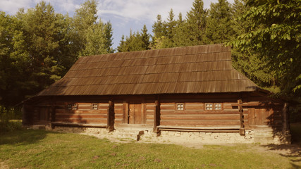 Fototapeta na wymiar Long log house is surrounded by trees. Meadow in front of the house.