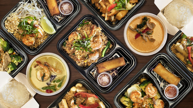 Variety of Thai food on wooden table. To go / delivery box.