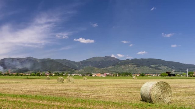 Beautiful view of the Tuscan countryside near Pisa with passage of smoke and clouds in the sky and Bientina and Monte Serra in the background and round hay bales. Time lapse motion