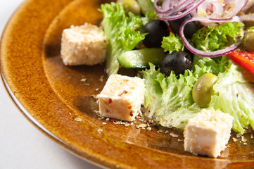 
Greek salad close-up. Healthy eating Olives, cheese, greens, lettuce, onions, tomatoes, appetizingly served on a brown plate