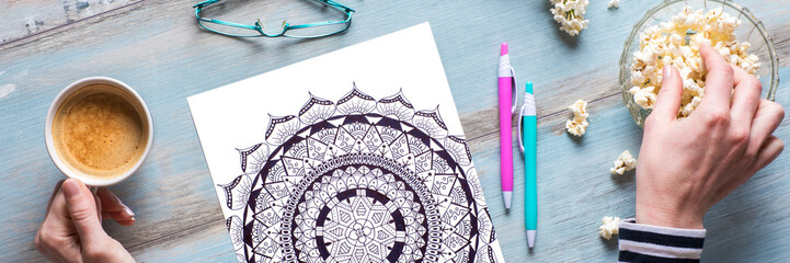 Adult coloring book, stress relieving trend. Art therapy, mental health, creativity and mindfulness concept. Flat lay close up on woman hands coloring an adult coloring book banner.