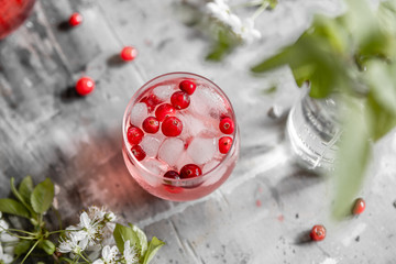 Top view spring cranberry lemonade in a glass on a gray shabby table with cherry flowers and leaves