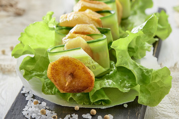 Sliced fried potatoes and cucumber on skewer on leaf of green lettuce on wooden Board.