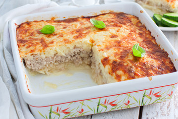 Potato casserole with minced meat in a square ceramic form on a wooden table, selective focus