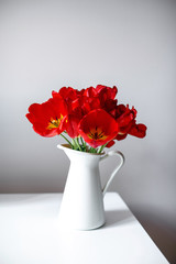 A beautiful bouquet of red tulips is standing in a white jug on the table. Festive bouquet as a gift. Focus on flowers. The concept of surprise.