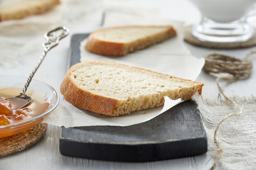 Breakfast with bread and fruit jam on wooden table on background of transparent Cup with milk in blur.
